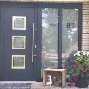 Moderne Haustür aus Anthrazit mit Glasfeldern, Hausnummer 83 und Blumendekoration.