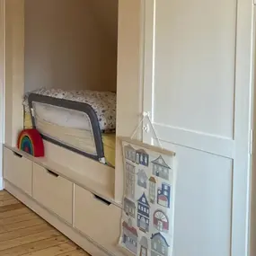 Kinderzimmer mit eingebautem Bett, Schubladen, Holzfußboden und bunter Dekoration.