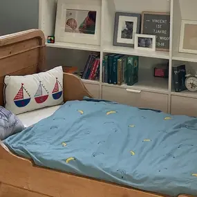 Holzbett im Kinderzimmer mit blauer Bettdecke, Bücherregal und dekorativen Kissen.