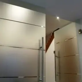 Zwei moderne, satinierte Glastüren mit Edelstahlgriffen in einem hellen Flur.