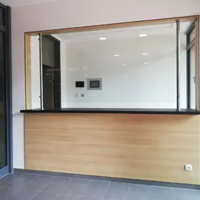 Moderne Empfangstheke mit Glasfenster und Holzverkleidung in einem hellen Eingangsbereich.