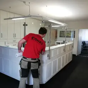 Handwerker montiert transparente Schutzwand an weißem Empfangstresen in modernem Büro.