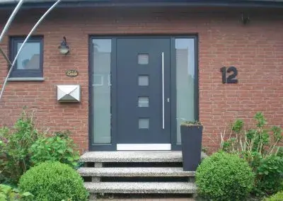 Moderne Haustür aus Glas und Metall in einem roten Klinkerhaus mit Hausnummer 12.