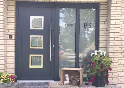 Moderne Haustür aus Anthrazit mit Glasfeldern, Hausnummer 83 und Blumendekoration.