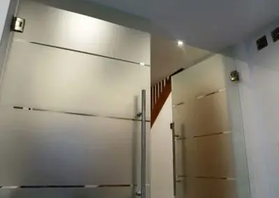 Zwei moderne, satinierte Glastüren mit Edelstahlgriffen in einem hellen Flur.