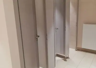 Mehrere geschlossene und teilweise geöffnete Toilettenkabinen in einer öffentlichen Toilette.